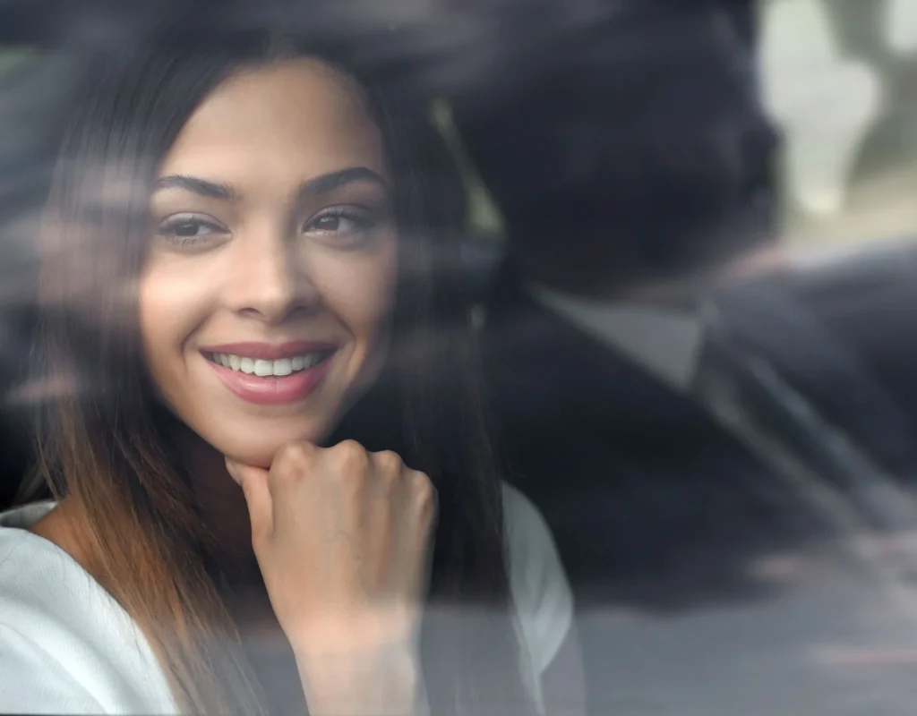 A smiling woman enjoying a luxurious chauffeur-driven ride with a professional driver in the background.