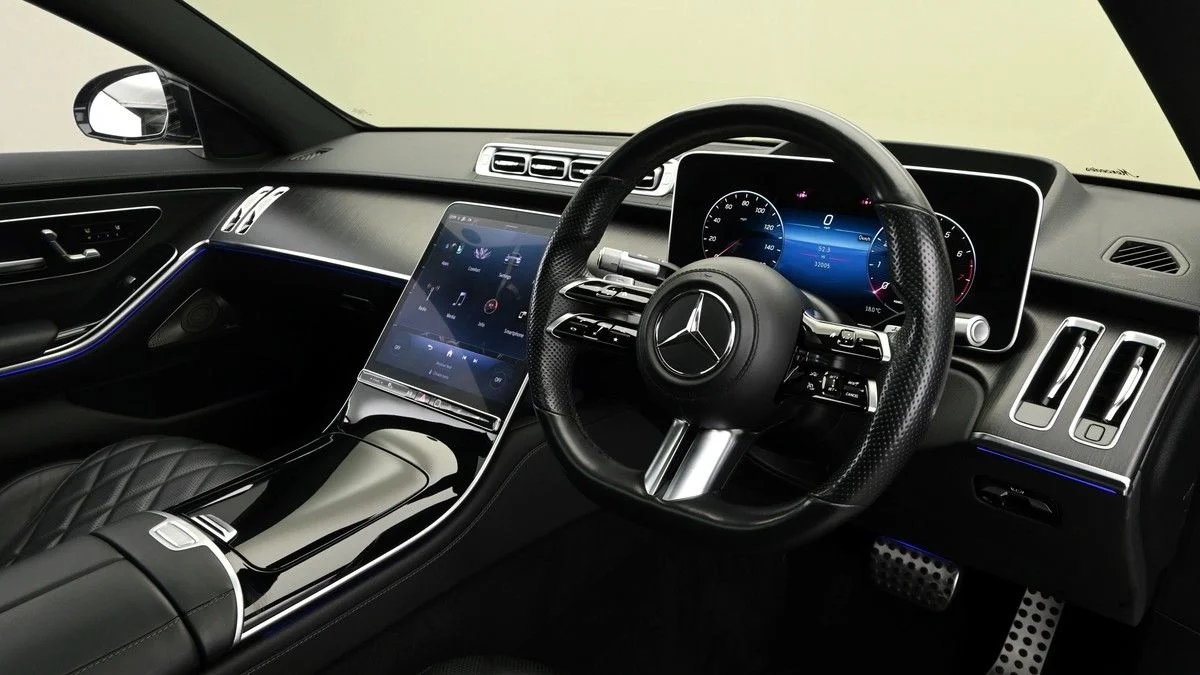 A business professional with silver hair and glasses sitting comfortably inside a luxury Mercedes-Benz S-Class, working on her laptop.